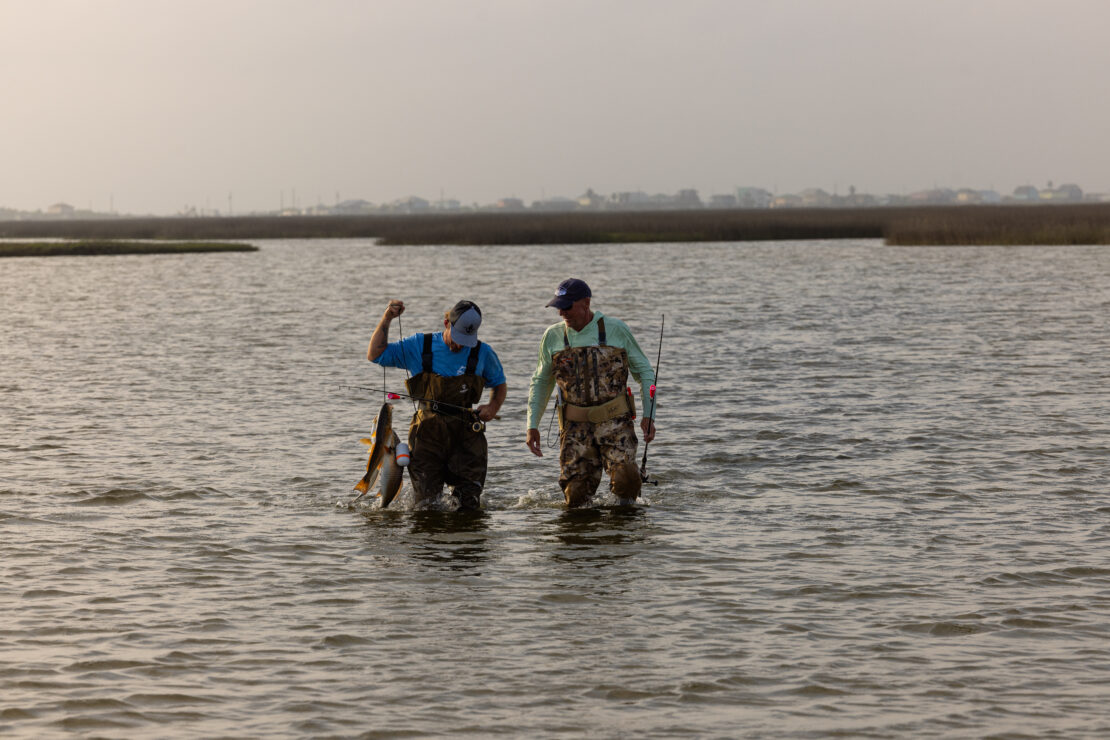 Two fishermen walking through the water in the wetlands of Matagorda Bay Nature Park while carrying fish.