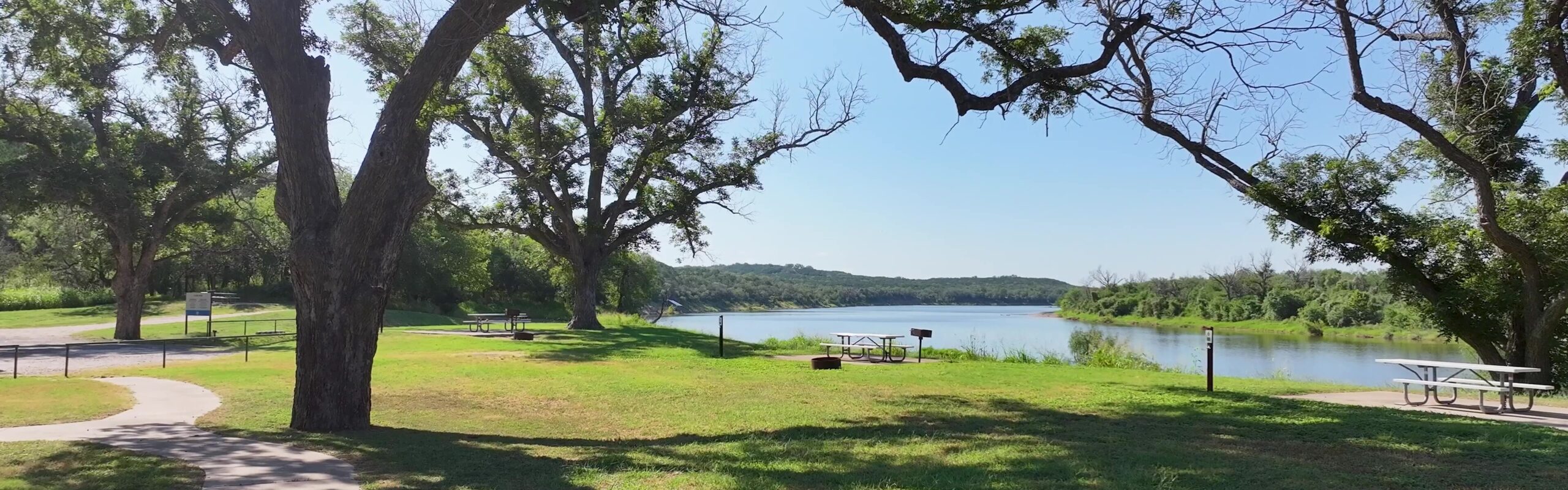 A group of grassy campsites. Green grass and trees in front of a wide lake.